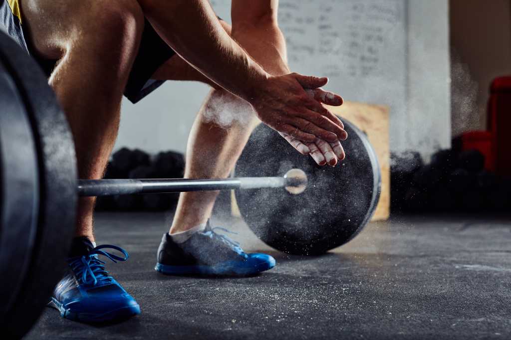 Closeup of weightlifter crouched and clapping hands together before barbell workout at the gym.