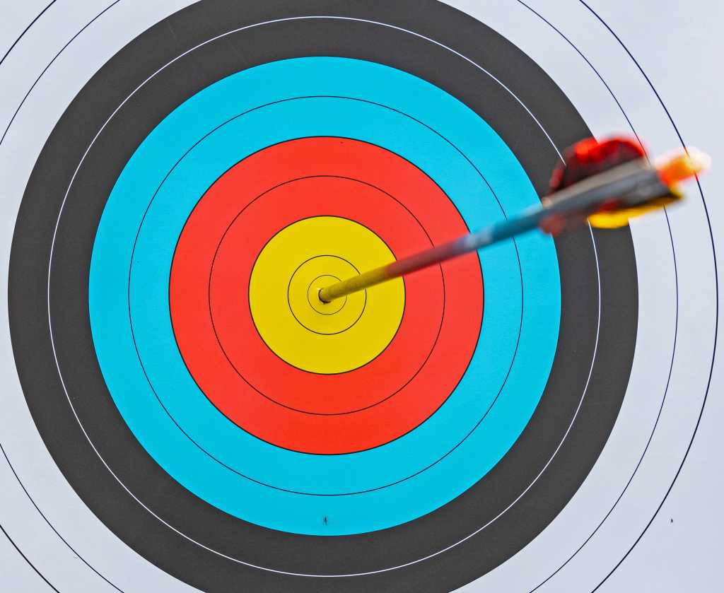 close-up view of archery target with yellow red blue black and white rings and arrow at the center - bullseye accuracy
