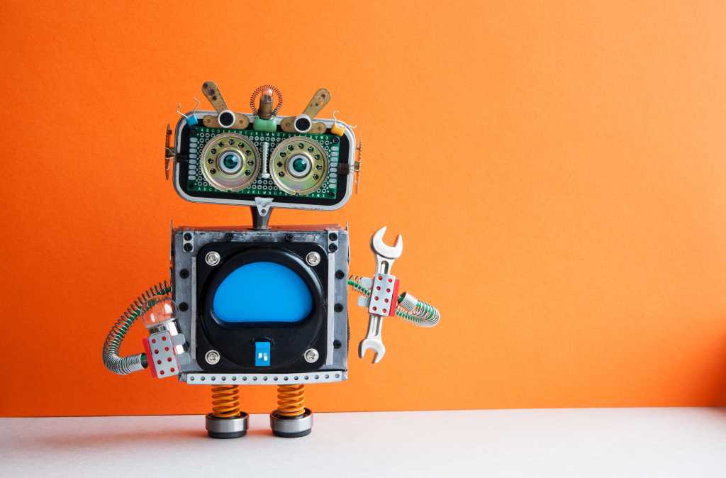 Cute little robot toy handyman mechanic with hand wrench and light bulb standing on a white floor with orange background. Fix repair maintenance concept.