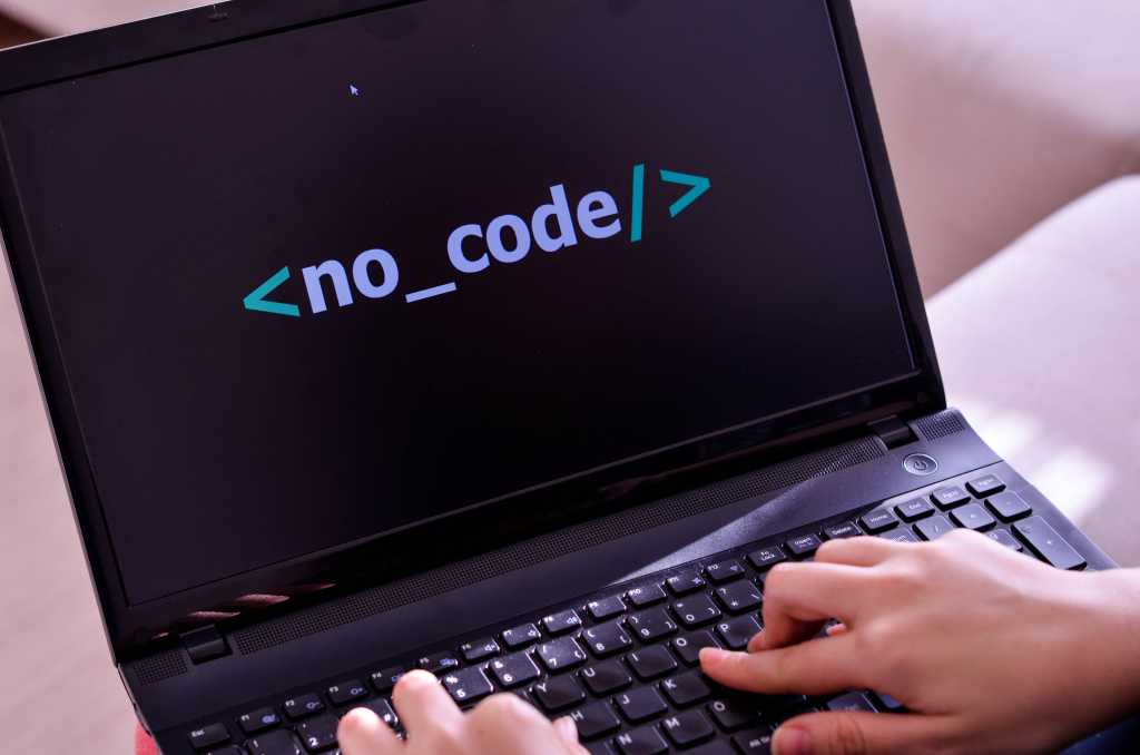 A person at an open laptop with the words "no code" displayed on the screen.