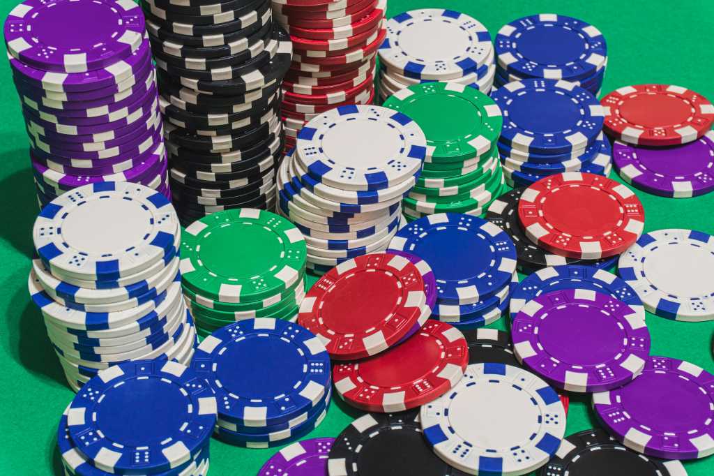 stacks of red white blue green black purple casino chips or betting chips on green gambling or gaming table