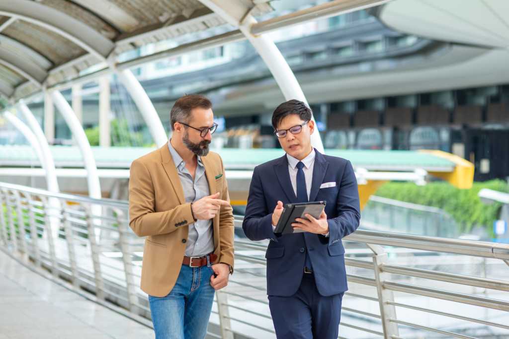 Two Businessman working corporate business and financial on digital tablet and discussion business plan during walking in the city. Business people entrepreneur partnership meeting outside office.
