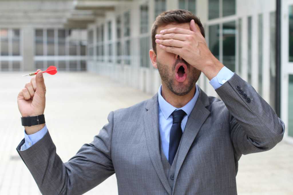 Businessman with one hand over his eyes holding a red dart. Flying blind.