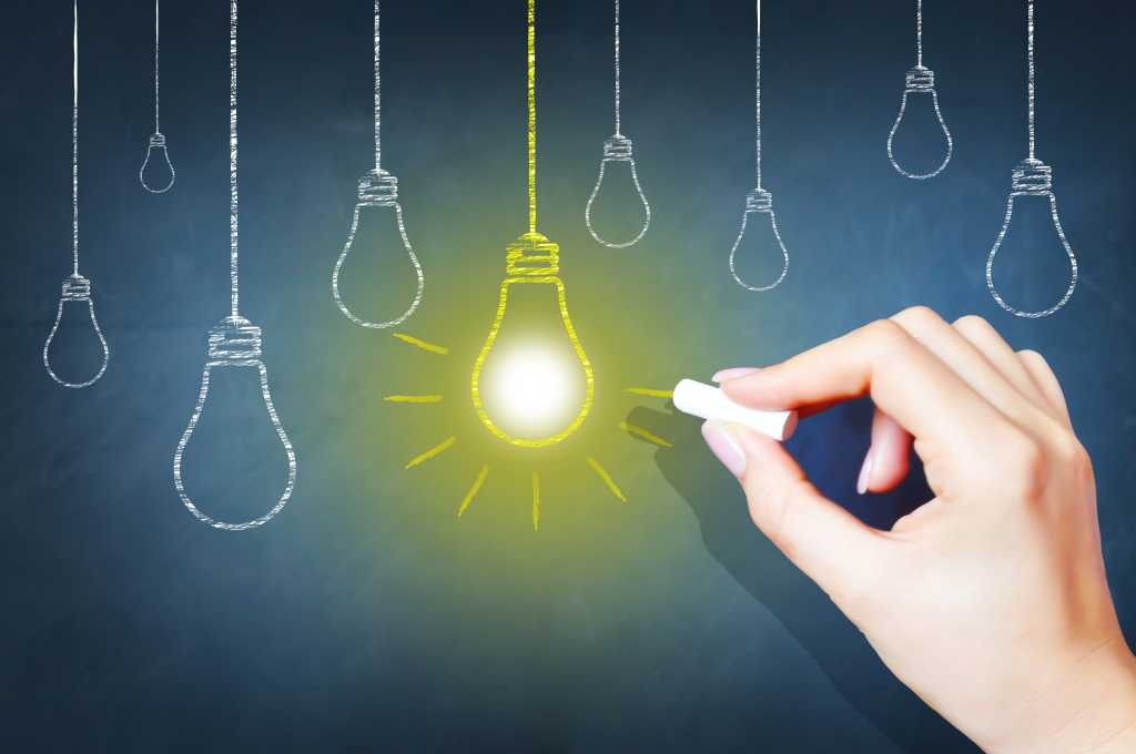 A hand draws a series of hanging lightbulbs and one of them is bright yellow.